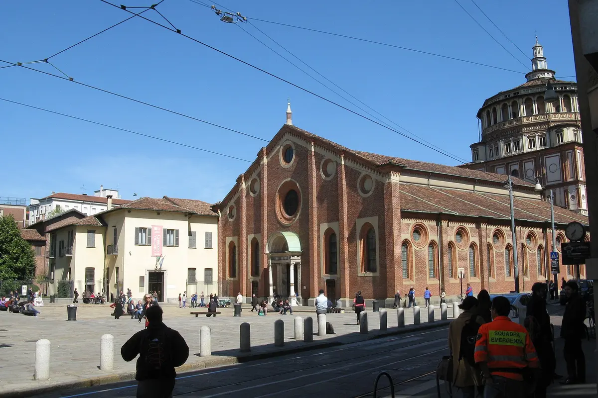 Piazza Santa Maria delle Grazie in Milan, with the brick church and its domed apse at the centre and a pale building with a Cenacolo Vinciano banner on the left